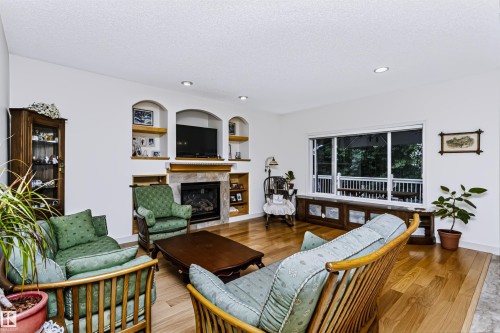 Recessed lighting, wood-finish flooring, built-in fireplace with stone surround, custom wall niches with shelving, and a large window with built-in storage bench - 1720 Robertson Place Sw, Edmonton, AB - Indoor Photo Showing Living Room With Fireplace