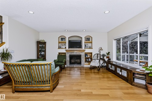 Hardwood flooring throughout, recessed ceiling lighting, stone-clad fireplace with mantel, built-in arched shelving, and large picture windows - 1720 Robertson Place Sw, Edmonton, AB - Indoor With Fireplace