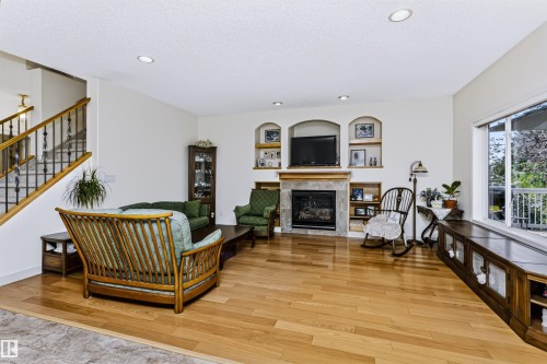 Hardwood flooring throughout, stone-clad fireplace, integrated shelving, and large window with built-in storage - 1720 Robertson Place Sw, Edmonton, AB - Indoor Photo Showing Living Room With Fireplace