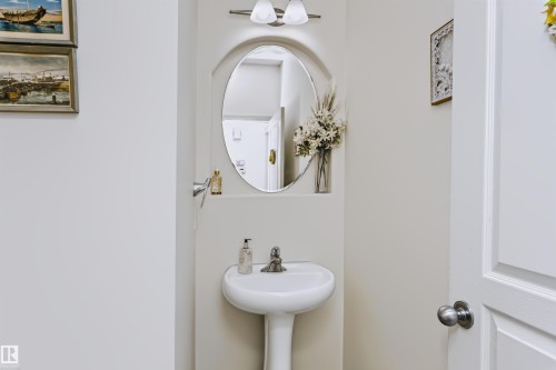 Pedestal sink with a polished chrome faucet, oval mirror, and wall-mounted vanity lighting - 1720 Robertson Place Sw, Edmonton, AB - Indoor Photo Showing Bathroom
