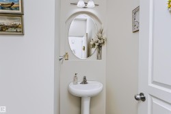 Pedestal sink with a polished chrome faucet, oval mirror, and wall-mounted vanity lighting - 