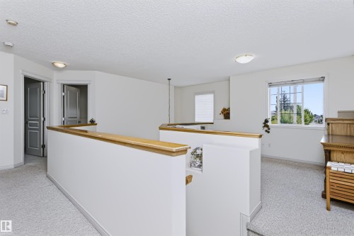 Carpeted landing with white walls, wood-capped half walls, and a large window with gridded panes - 1720 Robertson Place Sw, Edmonton, AB - Indoor Photo Showing Other Room