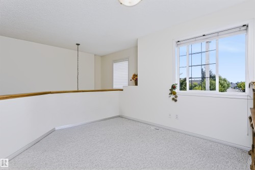 Carpeted open area with a wood-top half wall, white window blinds, and a multi-pane window - 1720 Robertson Place Sw, Edmonton, AB - Indoor Photo Showing Other Room