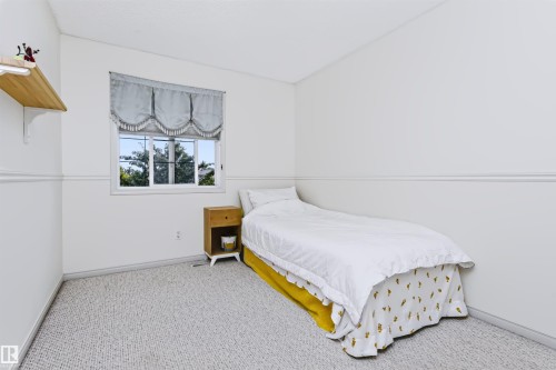 White walls, window with trim, wall molding, light-colored carpet flooring, and a built-in wood shelf - 1720 Robertson Place Sw, Edmonton, AB - Indoor Photo Showing Bedroom