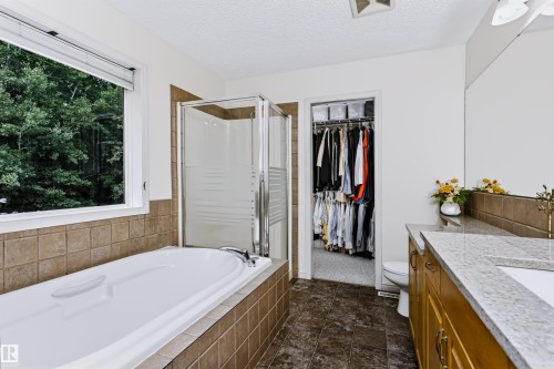 Integrated soaking tub with tiled surround, glass-enclosed shower, dual vanity with light-toned countertop, and an adjacent walk-in closet - 1720 Robertson Place Sw, Edmonton, AB - Indoor Photo Showing Bathroom