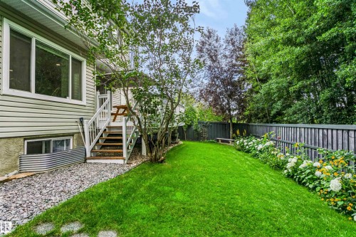 Expansive green lawn, mature trees, flowering garden beds, privacy fencing, and a multi-level deck with stairs - 1720 Robertson Place Sw, Edmonton, AB - Outdoor