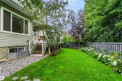 Expansive green lawn, mature trees, flowering garden beds, privacy fencing, and a multi-level deck with stairs - 