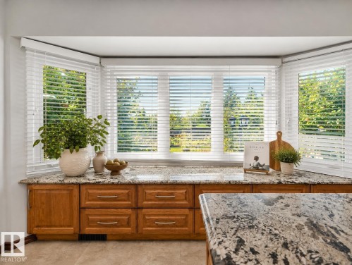 Bright bay window featuring multiple panes of plantation shutters, polished stone countertop, and warm wood-finish cabinetry with integrated drawer storage - 7357 18 Avenue Nw, Edmonton, AB - Indoor