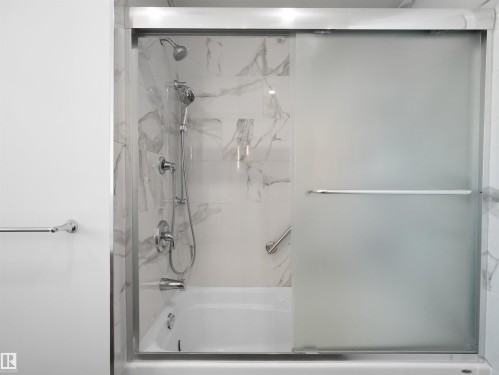Modern shower enclosure featuring frameless glass doors, dual showerheads with adjustable spray patterns, chrome fixtures, and marble-look tile surround with integrated shelving - 7357 18 Avenue Nw, Edmonton, AB - Indoor Photo Showing Bathroom