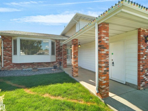 Brick and rendered facade with covered carport entry, white garage door, and manicured front lawn - 7357 18 Avenue Nw, Edmonton, AB - Outdoor