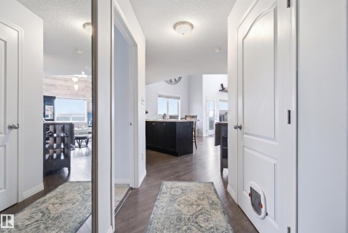 Hallway featuring wood-finish flooring, white paneled doors, and a full-length mirrored closet door - #2415 9357 Simpson Dr Nw, Edmonton, AB - Indoor Photo Showing Other Room