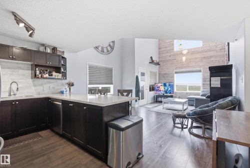 Open-concept living area with wood-finish flooring, a kitchen island with stone-finish countertop, dark cabinetry, and a subway tile backsplash - #2415 9357 Simpson Dr Nw, Edmonton, AB - Indoor Photo Showing Kitchen