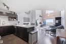 Open-concept living area with wood-finish flooring, a kitchen island with stone-finish countertop, dark cabinetry, and a subway tile backsplash - #2415 9357 Simpson Dr Nw, Edmonton, AB  - Indoor Photo Showing Kitchen 