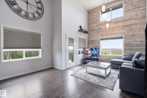 Vaulted ceiling with decorative wall clock, wood-finish flooring, accent wall with horizontal wood paneling, multiple windows with blinds, and a glass-paneled door - #2415 9357 Simpson Dr Nw, Edmonton, AB - Indoor