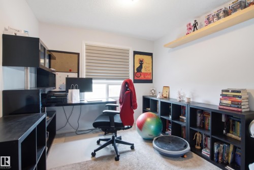 Built-in black storage shelving, integrated desk, light-toned wall paint, horizontal window blinds, and overhead lighting - #2415 9357 Simpson Dr Nw, Edmonton, AB - Indoor Photo Showing Office