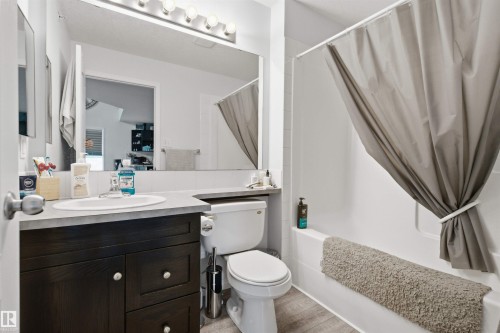 Wood-finish flooring, dark wood vanity with a white basin sink, polished chrome faucet, and a large mirror with overhead lighting - #2415 9357 Simpson Dr Nw, Edmonton, AB - Indoor Photo Showing Bathroom