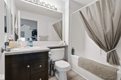 Wood-finish flooring, dark wood vanity with a white basin sink, polished chrome faucet, and a large mirror with overhead lighting - 