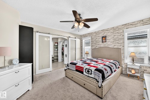 Textured accent wall, ceiling fan with integrated lighting, dual windows, carpeted flooring, and sliding barn doors with frosted panels - 4210 37 Avenue Nw, Edmonton, AB - Indoor Photo Showing Bedroom