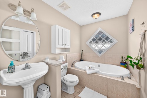 Pedestal sink with round mirror, built-in soaking tub with tiled surround, and glass block window - 4210 37 Avenue Nw, Edmonton, AB - Indoor Photo Showing Bathroom