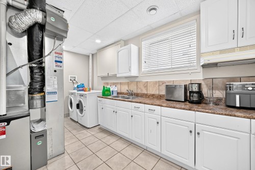 Laundry area featuring an HVAC system, tile flooring, white cabinetry, a double basin sink, and a window with blinds - 4210 37 Avenue Nw, Edmonton, AB - Indoor Photo Showing Laundry Room