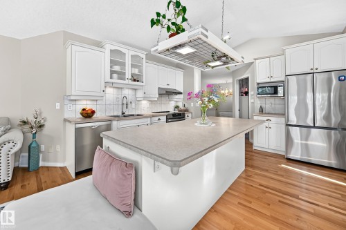 Kitchen featuring light wood-finish flooring, white cabinetry, stainless steel appliances, a center island with a light-toned countertop, and a vaulted ceiling - 4210 37 Avenue Nw, Edmonton, AB - Indoor Photo Showing Kitchen