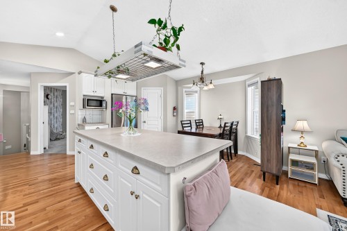Kitchen island with white cabinetry and light-toned countertop, hardwood flooring, white kitchen cabinetry with stainless steel appliances, bay window with natural light, and recessed lighting - 4210 37 Avenue Nw, Edmonton, AB - Indoor Photo Showing Kitchen With Double Sink