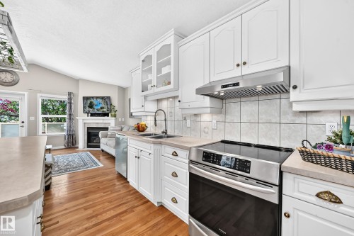 White cabinetry with glass-front accents, stainless steel appliances, light-toned countertops, and wood-finish flooring - 4210 37 Avenue Nw, Edmonton, AB - Indoor Photo Showing Kitchen With Double Sink With Upgraded Kitchen