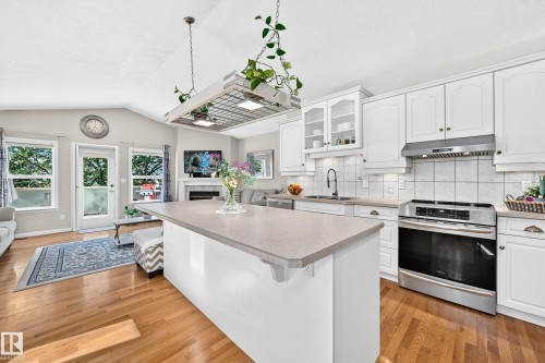 Open-concept kitchen featuring an island with countertop seating, white cabinetry, stainless steel appliances, and wood-finish flooring - 4210 37 Avenue Nw, Edmonton, AB - Indoor Photo Showing Kitchen With Upgraded Kitchen