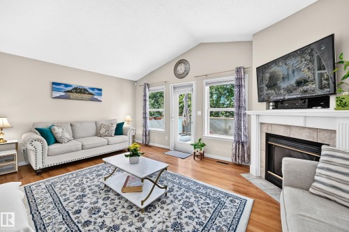 Vaulted ceiling, hardwood flooring, fireplace with tile surround, two large windows, and a glass-paneled door - 4210 37 Avenue Nw, Edmonton, AB - Indoor Photo Showing Living Room With Fireplace