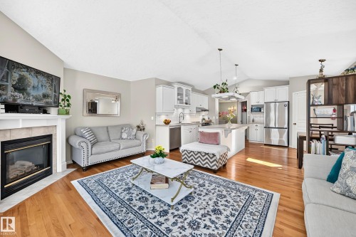 Open-concept living area with vaulted ceilings, hardwood flooring, a fireplace with a tile surround, white kitchen cabinetry, and stainless steel appliances - 4210 37 Avenue Nw, Edmonton, AB - Indoor Photo Showing Living Room With Fireplace