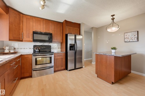 Wood-finish flooring, stainless steel appliances, wood cabinetry, stone countertops, and a kitchen island - 6768 39 Avenue Nw, Edmonton, AB - Indoor Photo Showing Kitchen