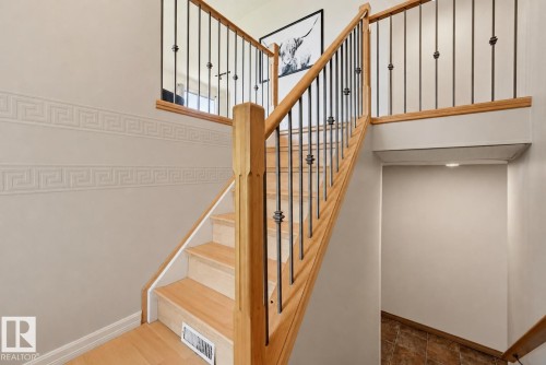 Wood-finish stairs with wrought iron balusters and a complementary wood handrail - 6768 39 Avenue Nw, Edmonton, AB - Indoor Photo Showing Other Room