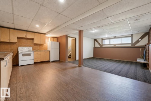 Open-concept living space featuring wood-finish flooring throughout, custom cabinetry with ample storage, white appliances including range and refrigerator, and recessed ceiling lighting - 6768 39 Avenue Nw, Edmonton, AB - Indoor