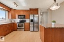 Kitchen featuring wood-finish cabinetry, stainless steel appliances, light-toned wood-finish flooring, and a central island with a stone-finish countertop - 6768 39 Avenue Nw, Edmonton, AB  - Indoor Photo Showing Kitchen With Stainless Steel Kitchen 