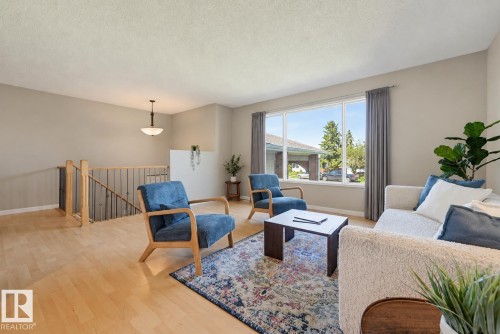 Neutral wall finishes, light wood-finish flooring, large window, built-in staircase with wood railing, and a ceiling-mounted light fixture - 6768 39 Avenue Nw, Edmonton, AB - Indoor Photo Showing Living Room