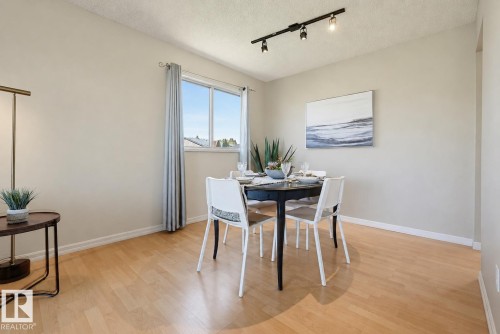 Light wood-finish flooring, track lighting, and a bright window with drapes - 6768 39 Avenue Nw, Edmonton, AB - Indoor Photo Showing Dining Room