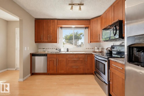 Kitchen featuring wood-finish cabinetry, light-toned wood-finish flooring, stainless steel appliances, and a window with a sink below - 6768 39 Avenue Nw, Edmonton, AB - Indoor Photo Showing Kitchen With Stainless Steel Kitchen