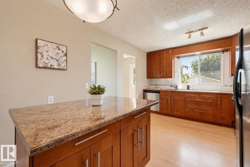 Kitchen featuring wood-finish flooring, wood cabinetry with brushed nickel hardware, and stone countertops - 6768 39 Avenue Nw, Edmonton, AB - Indoor Photo Showing Kitchen