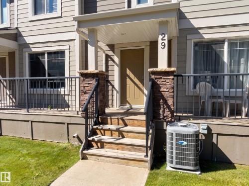Exterior featuring horizontal siding, a covered porch, stone veneer column accents, a security railing, and an outdoor HVAC unit - #29 1150 Windermere Wy Sw, Edmonton, AB 