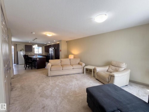 Open-concept living area with carpeting, recessed lighting, and a kitchen featuring dark wood cabinetry, an island, and stainless steel appliances - #29 1150 Windermere Wy Sw, Edmonton, AB 