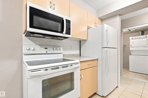 Kitchen featuring light wood-finish cabinetry, white appliances, and a tiled backsplash - #117 17011 67 Av Nw, Edmonton, AB - Indoor Photo Showing Kitchen