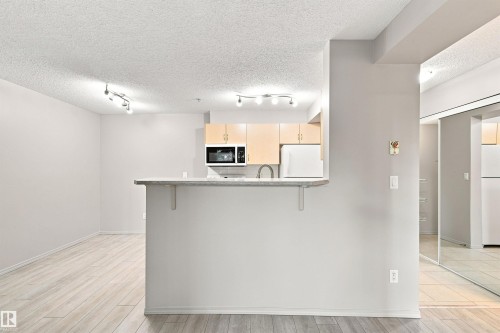 Open-concept kitchen with wood-finish cabinetry, built-in microwave, and a breakfast bar - #117 17011 67 Av Nw, Edmonton, AB - Indoor Photo Showing Kitchen
