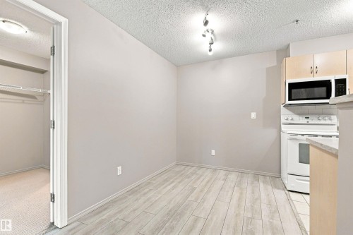 Wood-finish flooring throughout, white kitchen appliances, light wood-tone cabinetry, subway tile backsplash, and a built-in closet with wire shelving - #117 17011 67 Av Nw, Edmonton, AB - Indoor Photo Showing Kitchen