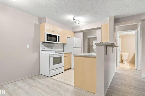 Kitchen featuring light wood-finish cabinetry, white appliances, and a tiled backsplash - #117 17011 67 Av Nw, Edmonton, AB - Indoor Photo Showing Kitchen