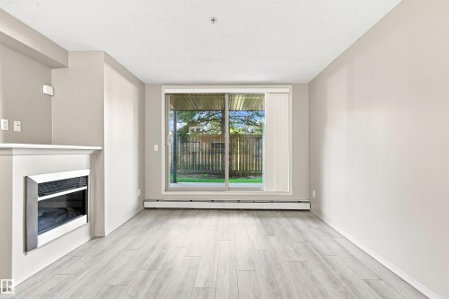 Wood-finish flooring, built-in fireplace, sliding glass door, and neutral wall tones - #117 17011 67 Av Nw, Edmonton, AB - Indoor With Fireplace
