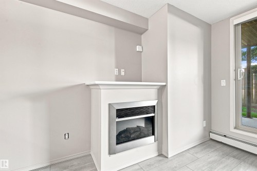 Electric fireplace with white mantel, light gray wall paint, light-toned wood-finish flooring, and sliding glass patio door - #117 17011 67 Av Nw, Edmonton, AB - Indoor With Fireplace