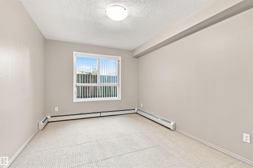 Recessed ceiling light fixture, neutral tone wall paint, textured carpet flooring, and a window with vertical blinds - #117 17011 67 Av Nw, Edmonton, AB - Indoor Photo Showing Other Room