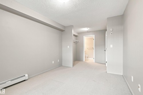 Carpeted flooring with light neutral wall paint, overhead lighting, and baseboard heating - #117 17011 67 Av Nw, Edmonton, AB - Indoor Photo Showing Other Room
