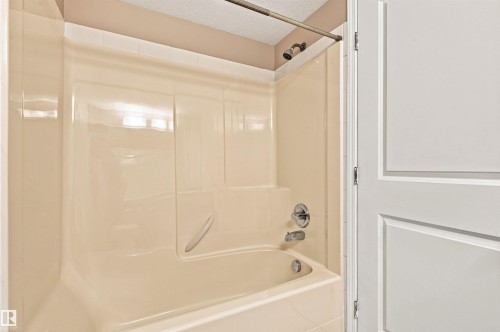 Bathtub with integrated shower surround, chrome showerhead, and matching chrome fixtures - #117 17011 67 Av Nw, Edmonton, AB - Indoor Photo Showing Bathroom