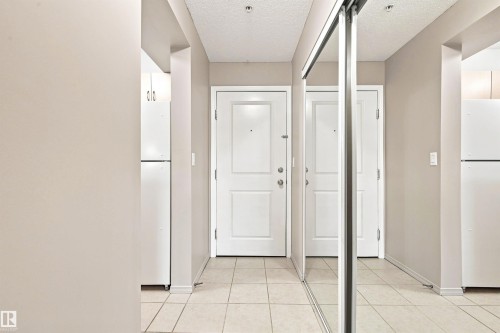 White paneled doors, mirrored sliding closet doors, tiled flooring, and light neutral wall tones - #117 17011 67 Av Nw, Edmonton, AB - Indoor Photo Showing Other Room